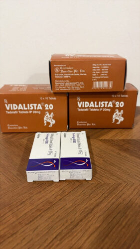 Brown boxes labeled Vidalista 20 tadalafil tablets on a wooden table with two white blister-pack boxes in front.