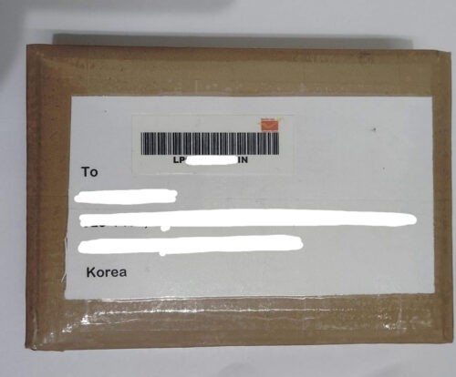 Brown cardboard shipping box with a white label showing a barcode and partially redacted recipient info; appears to be addressed to Korea.