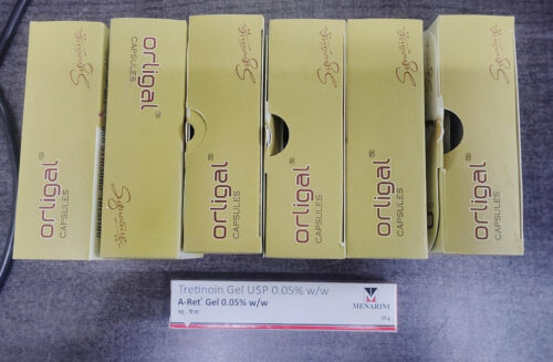 Six pale-yellow boxes labeled something like '... Capsules' arranged in a row on a gray surface, with a white-and-red tretinoin gel box at the front bottom.