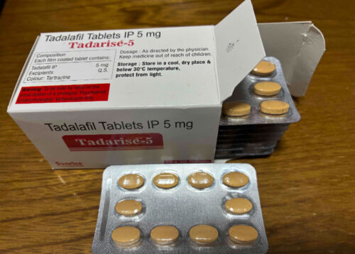 Box of Tadalafil tablets labeled Tadarise-5 IP 5 mg with round tan pills in blister packs on a wooden surface.