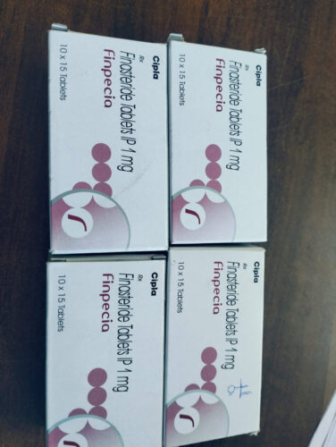 Boxes of Cipla Finasteride tablets IP 1 mg (10 x 15 tablets) arranged on a wooden surface.