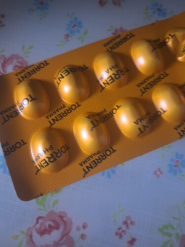 Close-up of yellow oval tablets in a yellow blister pack on a floral tablecloth.