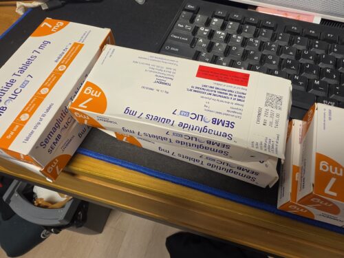 Boxes of medicine with orange-and-white packaging showing '7 mg' on the box, placed on a desk next to a computer keyboard.