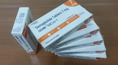 Boxed Semaglutide tablets 7 mg (Semblic 7) with orange and white packaging stacked on a wooden surface, showing multiple boxes.
